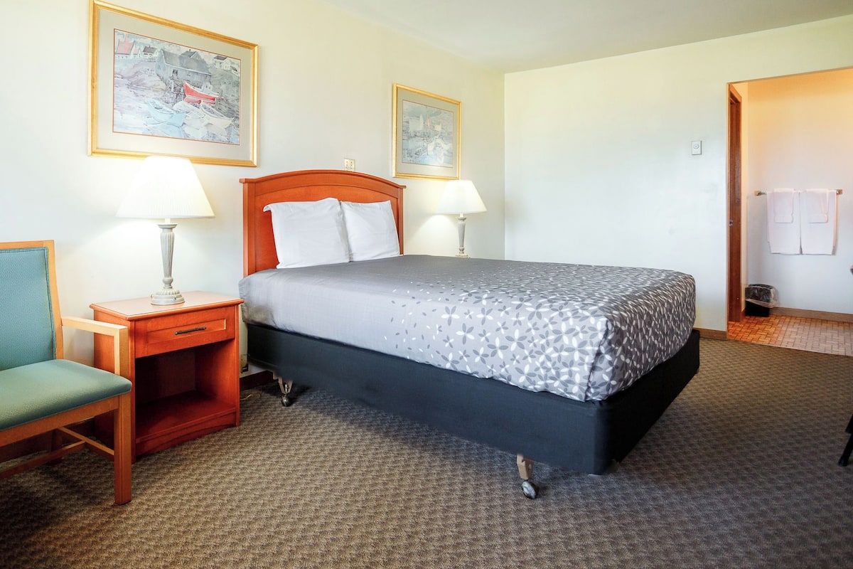 A hotel room with a bed, two bedside tables with lamps, a chair, and two framed pictures on the wall.
