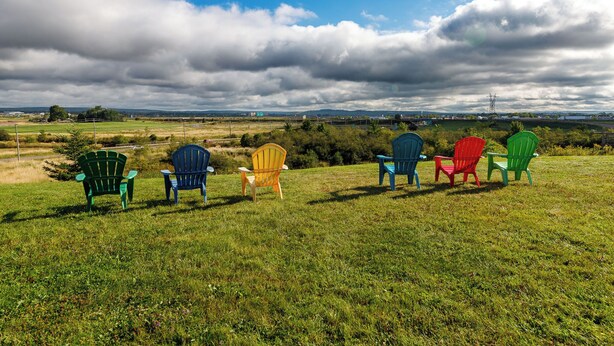 Un campo cubierto de césped con varias sillas Adirondack de colores que miran hacia un paisaje distante.
