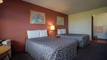 Ein Hotelzimmer mit zwei Betten, einem Schreibtisch, einer Lampe und zwei gerahmten Bildern an der Wand.