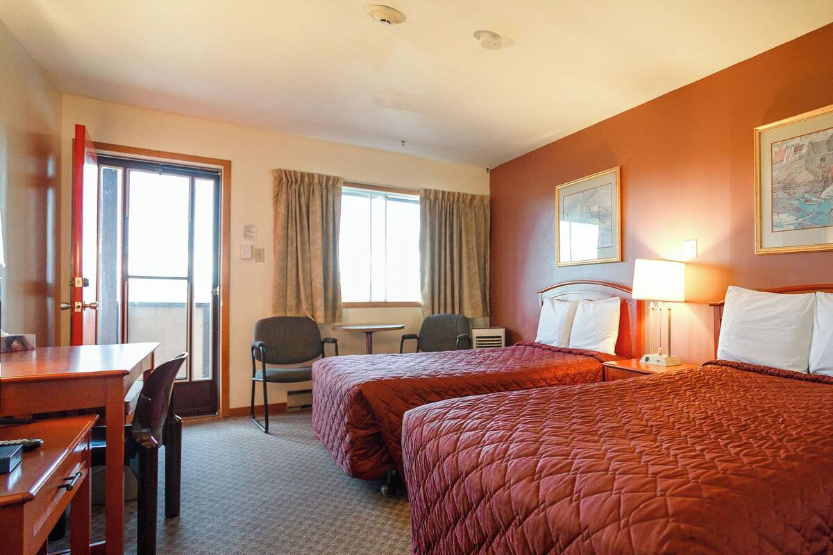 A hotel room with two beds, a desk, a chair, a table, and a window with curtains.