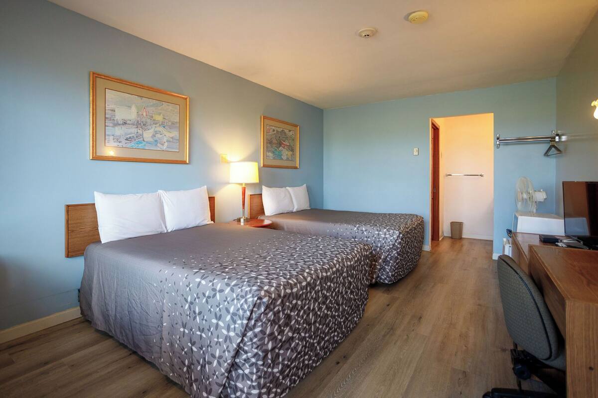 A hotel room with two beds, a desk, a chair, a lamp, and two framed pictures on the wall.