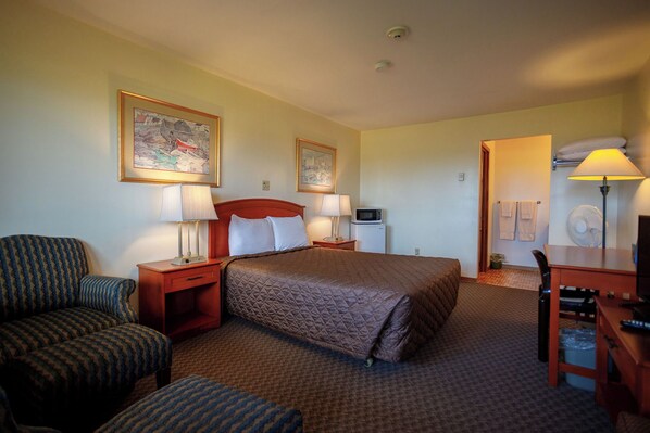 A hotel room with a bed, two chairs, a desk, a lamp, a television, and artwork on the walls.