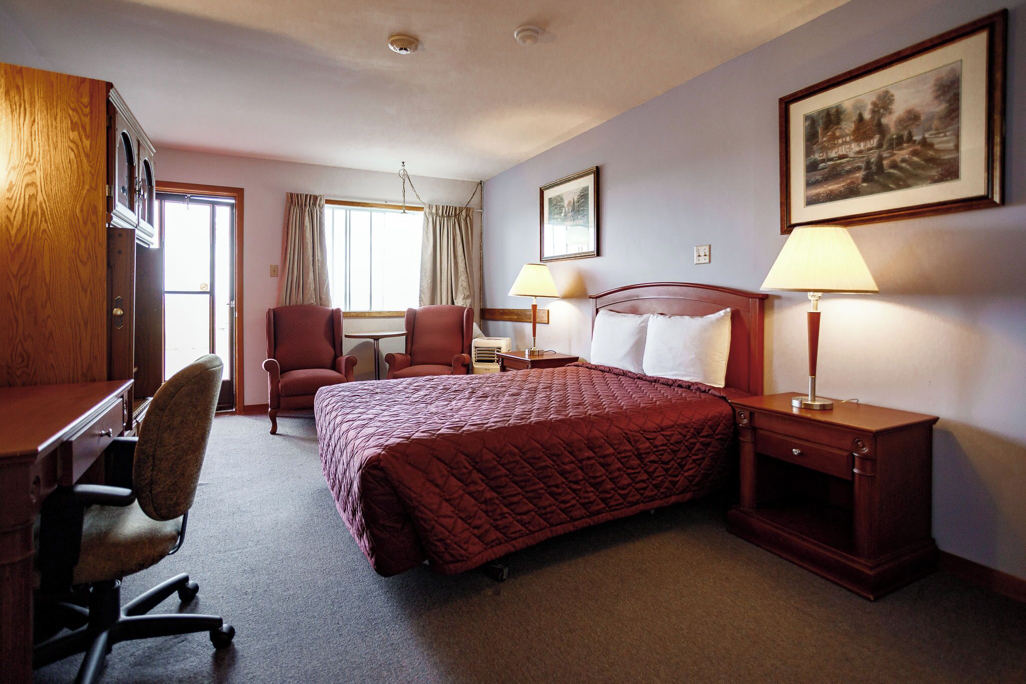 A hotel room with a bed, desk, chair, and two bedside tables with lamps.