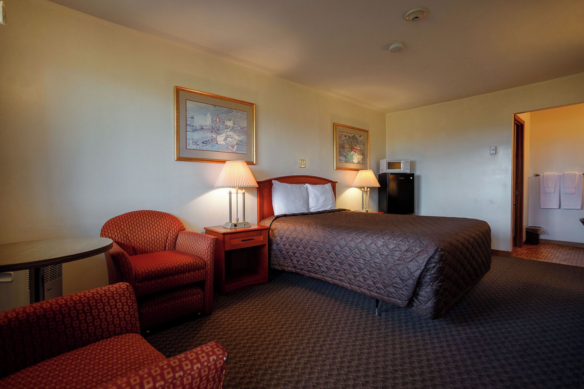 A hotel room with a bed, two chairs, a small table, two wall-mounted lamps, and a microwave.