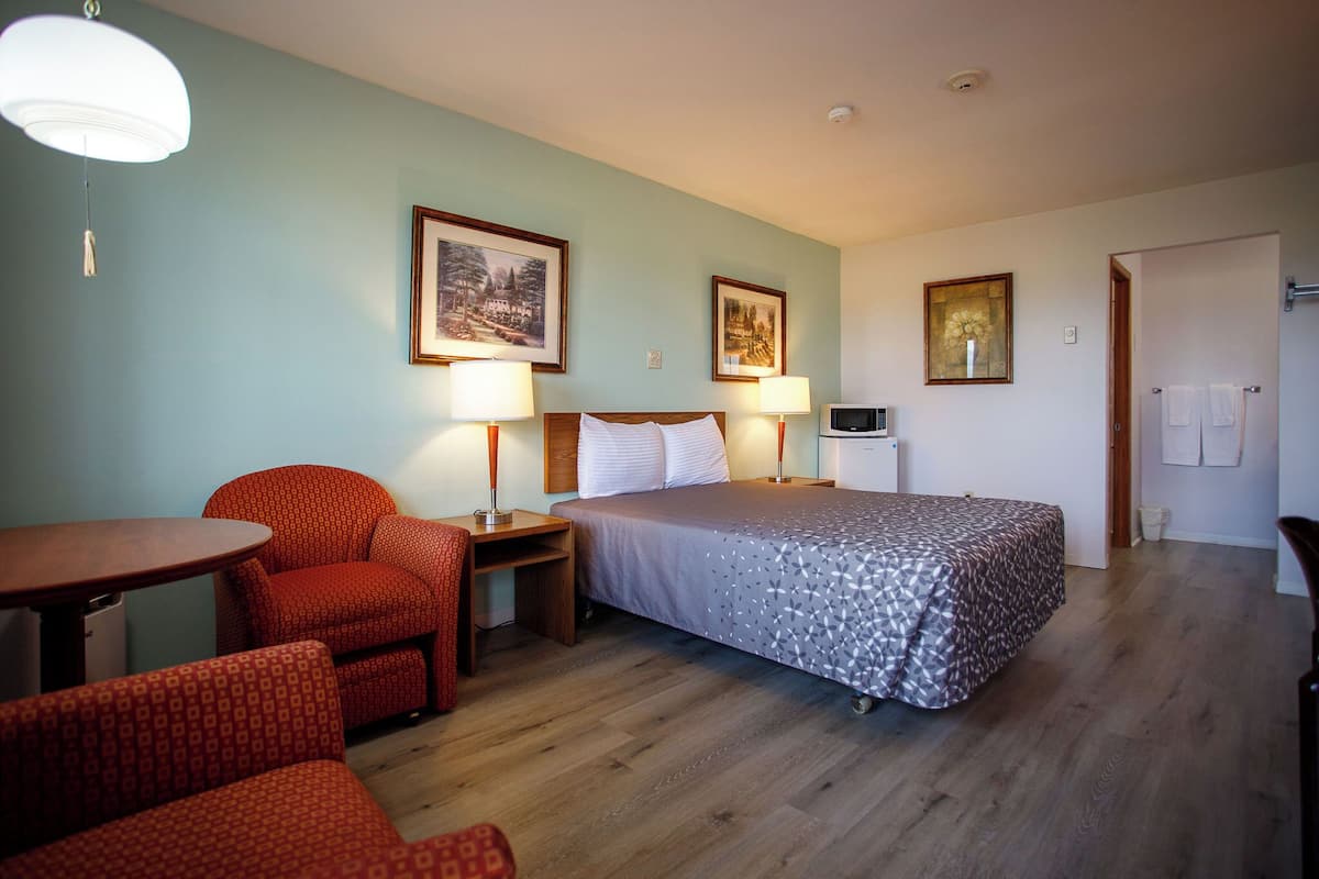 A hotel room with a bed, two chairs, a table, and a microwave.