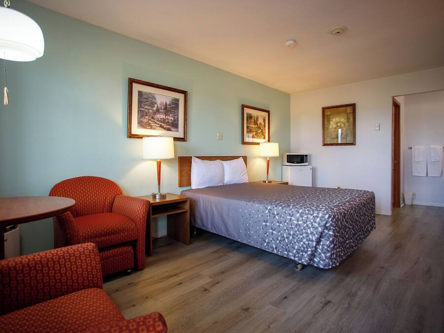 A hotel room with a bed, two chairs, a table, and a microwave.