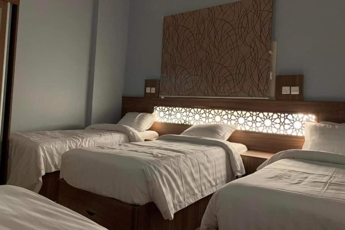 A hotel room with four single beds, a decorative wall panel, and a window with a geometric pattern.