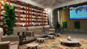 A lounge area with sofas, a coffee table, and a large screen displaying a sports event. - Aya Hostel For Shared Bedrooms (Madinah)