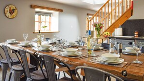 A dining area with a wooden table set for a meal, a wooden staircase, and a window with a view. - The Stables - UK45090 (Longdyke, near Morpeth)