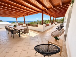 An outdoor patio with a wooden pergola, a dining table with chairs, and a view of the sea.