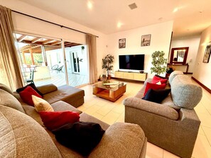 Een moderne woonkamer met een grote flatscreen-tv, comfortabele banken en een schuifdeur naar een buitenruimte.