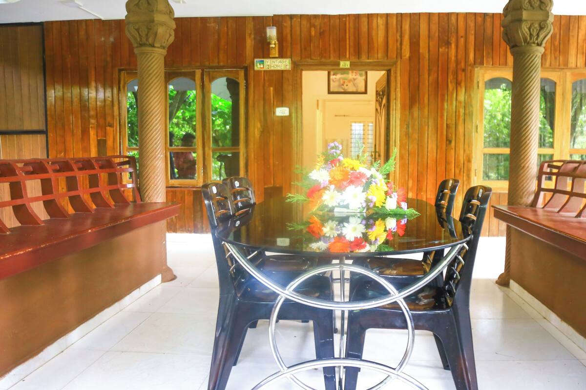 A dining area with a glass table surrounded by chairs, wooden paneling on the walls, and a floral centerpiece.