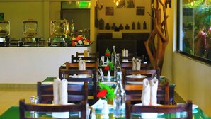 Un restaurant amb caires i taules de fusta preparades per dinar, una zona de bar amb vidrieres, i un element decoratiu a la paret.