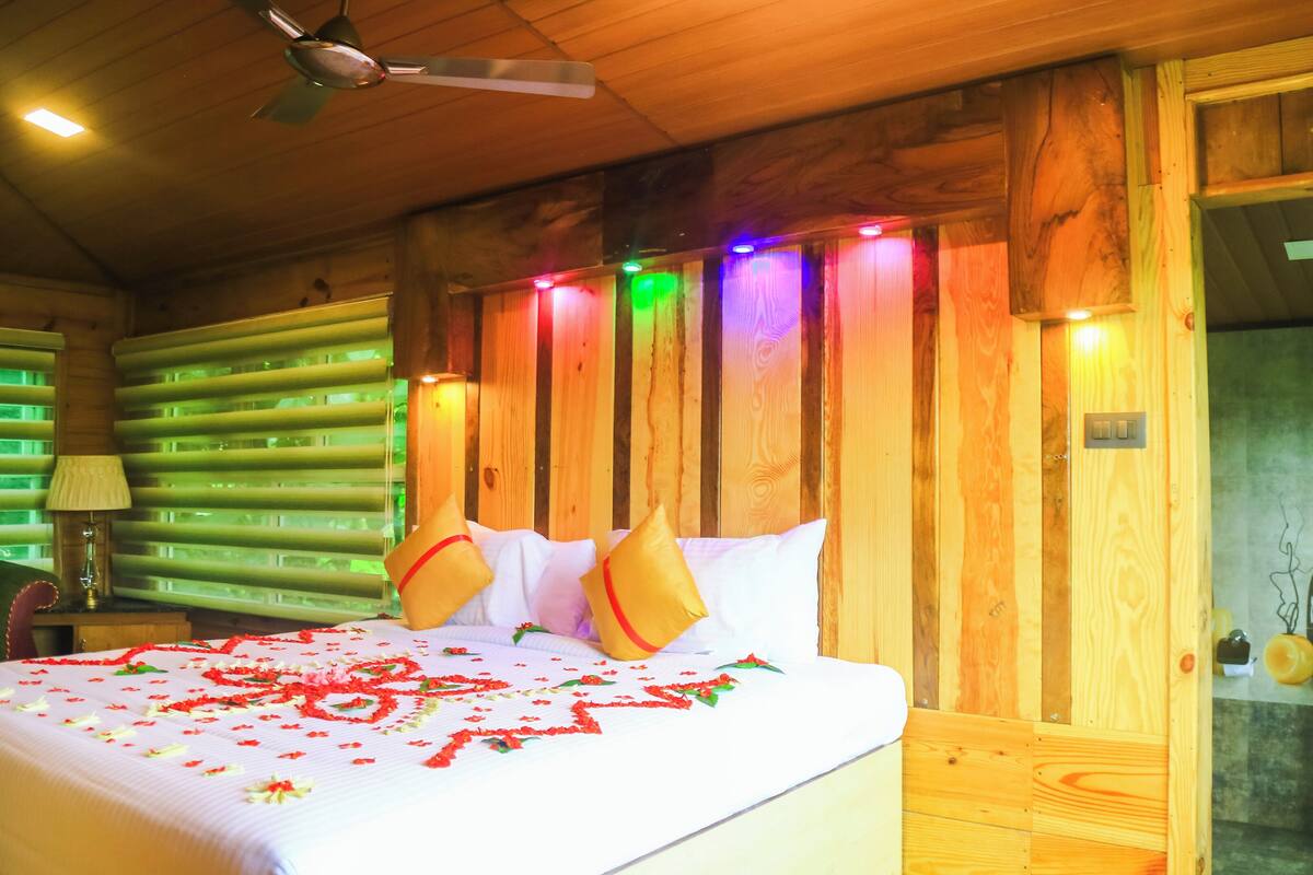 A wooden room with a bed, a ceiling fan, and a bathroom with a sink and mirror.