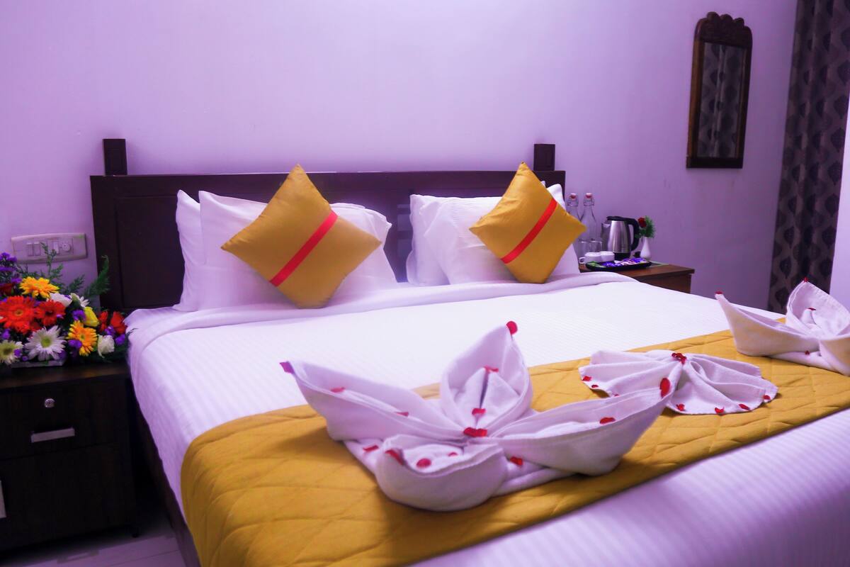 A neatly made bed with white linens and yellow pillows, a bedside table with a floral arrangement, and a bedside lamp.