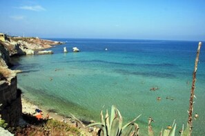 Een kustgezicht met helder turquoise water, rotskliffen en schaarse begroeiing.
