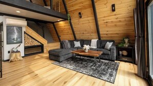 A modern loft-style living room with a wooden ceiling, a gray sectional sofa, a wooden coffee table, and a fireplace. - Thor’s Cabin luxury pet-friendly A-Frame w/ hot/cold tub & sauna 15 min to GSMNP (Cosby)