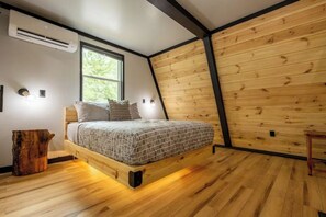 Un dormitorio con estructura de cama de madera, una ventana y pared de madera.