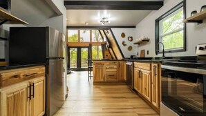 A modern kitchen with wooden cabinets, stainless steel appliances, and a large window providing natural light. - Thor’s Cabin luxury pet-friendly A-Frame w/ hot/cold tub & sauna 15 min to GSMNP (Cosby)