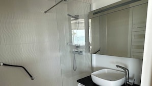 Un bany modern amb una cabina de dutxa de vidre, un lavabo blanc amb taulell negre i un mirall gran sobre el lavabo.