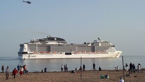 Un gran vaixell de creuer amarrat en un port, amb persones a la platja propera.