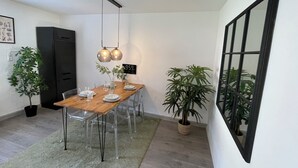 Uma sala de jantar com uma mesa de madeira, cadeiras transparentes, uma pequena planta em vaso e uma luminária pendente moderna.