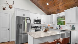 Una cocina moderna con armarios blancos, electrodomésticos de acero inoxidable y techo de madera.