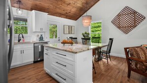 Una cocina con armarios blancos, techo de madera y zona de comedor con mesa y sillas.