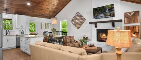 A spacious living area with a fireplace, a ceiling fan, and a dining area with a view of the outdoors.
