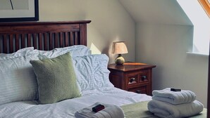 A neatly made bed with pillows, a bedside lamp, a nightstand with a lamp, and a window with a view. - Bracken Cottage - sleeps 4 guests  in 2 bedrooms (Argyll)