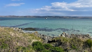 Un paysage côtier caractérisé par une eau turquoise et limpide, des rivages rocheux et des collines lointaines, le tout sous un ciel partiellement nuageux.