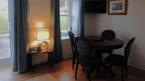 Un coin repas avec une table ronde, quatre chaises, une lampe, une horloge et un téléviseur fixé au mur.