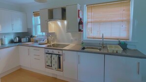 Eine moderne Küche mit weißen Schränken, einem eingebauten Backofen, einer Spüle und einem Fenster mit Jalousien.