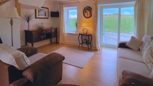 Ein Wohnzimmer mit Sofa, Tisch, Lampe und Blick ins Freie.