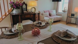 A dining area with a table set for four, a clock, a lamp, and a television mounted on the wall. - Foxglove Cottage - sleeps 4 guests  in 2 bedrooms (Argyll)