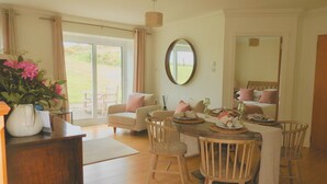 A dining area with a table set for four, a sofa, a chair, and a vase with flowers. - Foxglove Cottage - sleeps 4 guests  in 2 bedrooms (Argyll)