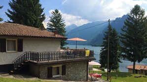 Una casa con fachada de piedra, un balcón con barandilla y vistas a un lago y montañas.