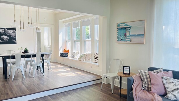 A spacious living area with a dining table, chairs, a sofa, and a window seat with cushions.