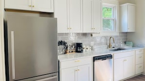 A modern kitchen with white cabinets, stainless steel appliances, and a window providing natural light.