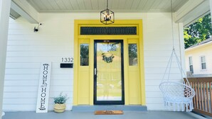 A yellow front door with a black glass panel, a hanging light fixture, and a mailbox labeled "1332".