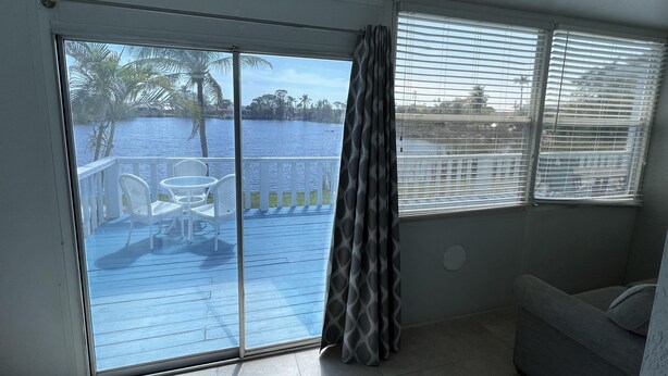 A room with a sliding glass door leading to a balcony with a view of a lake and palm trees. - Lakeview Superior Two-Bedroom Suite (Marco Island)