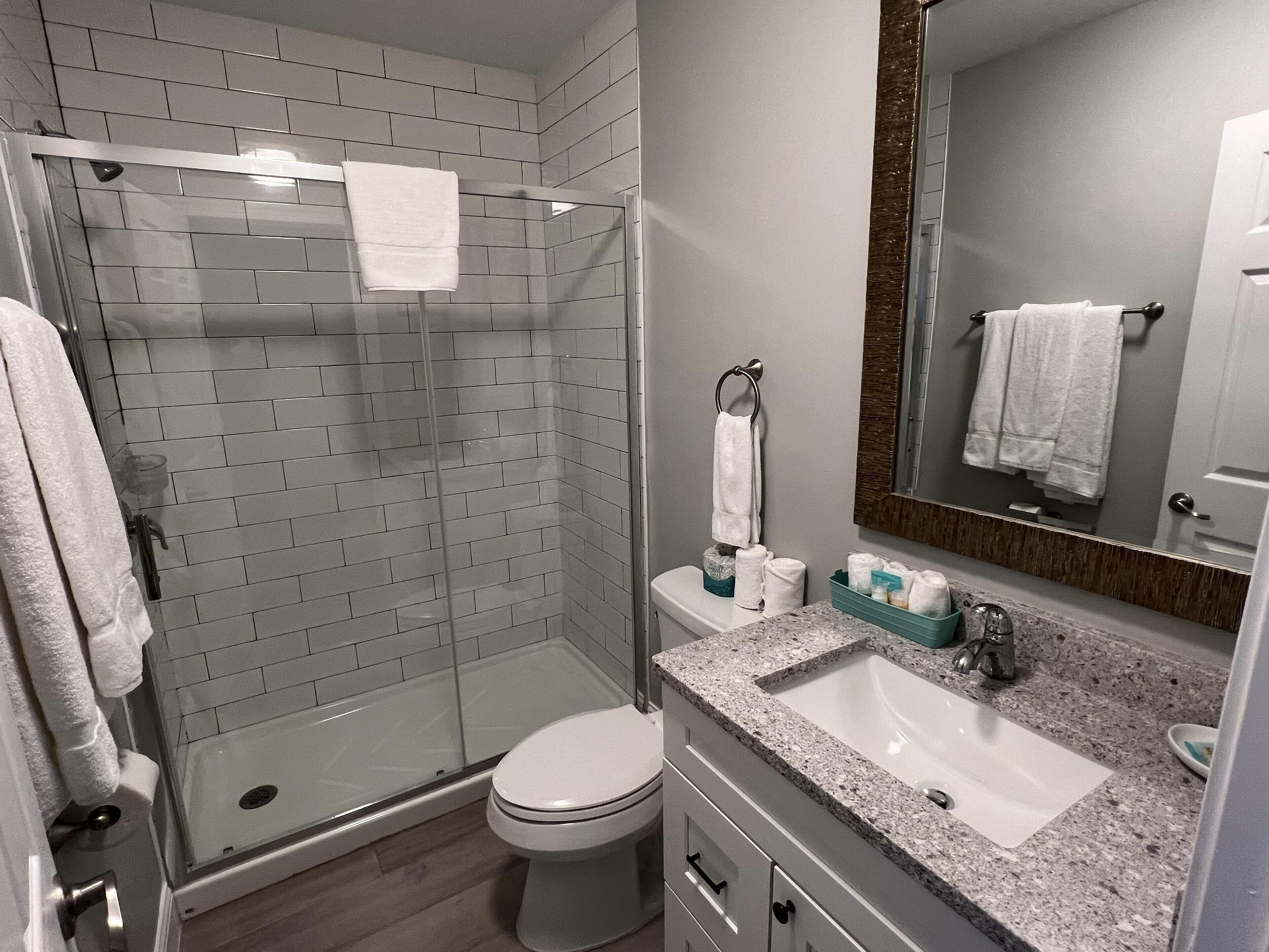 Un baño moderno con cabina de ducha de vidrio, inodoro, lavabo con espejo y toallero.