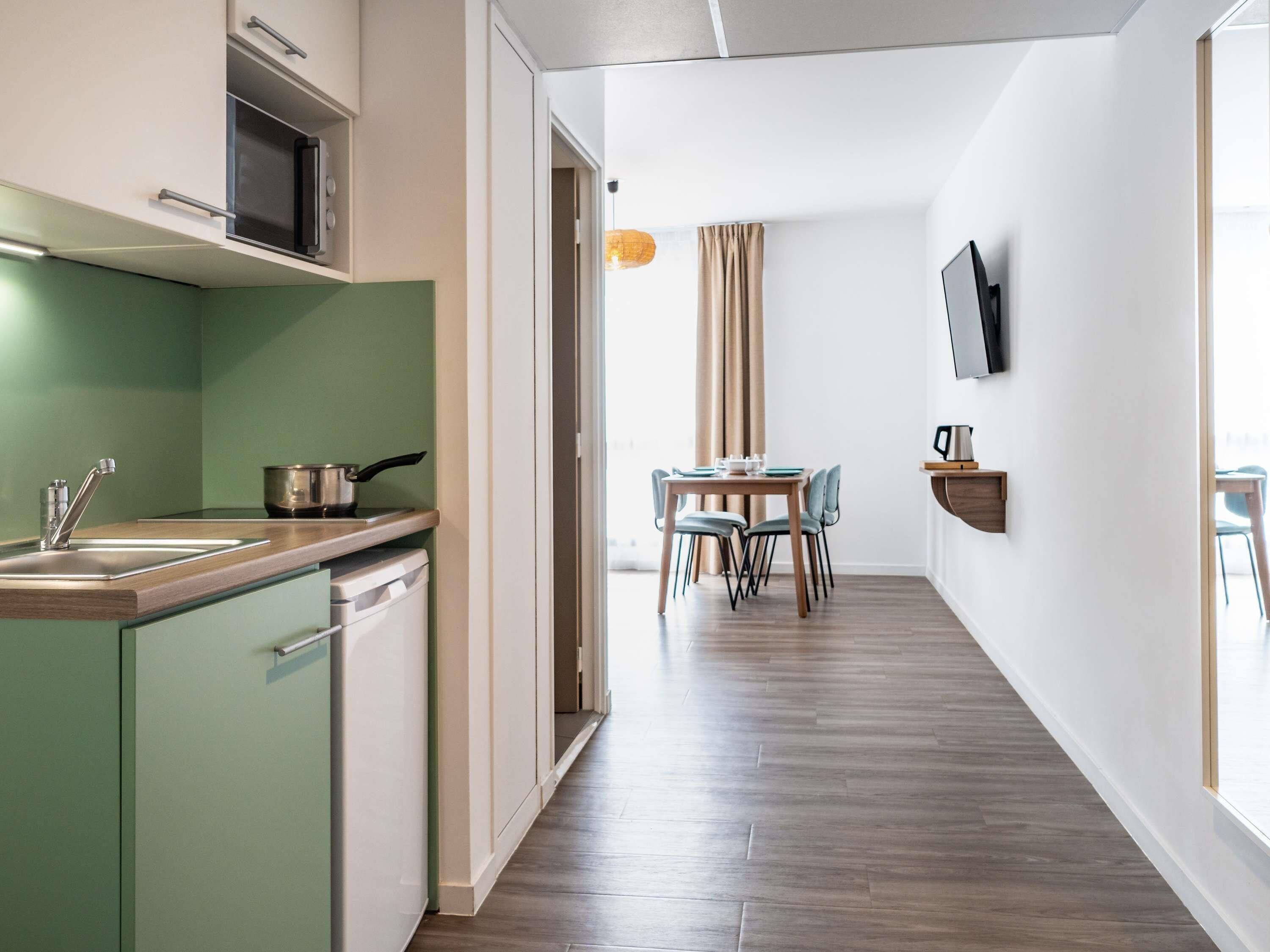 Una cocina moderna con microondas, estufa y pileta. Hay una zona de comedor con una mesa y sillas, y un televisor montado en la pared.