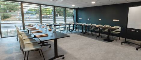Ein Konferenzraum mit einem langen Tisch, mehreren Stühlen, einer Tafel und großen Fenstern mit Blick auf die Straße.