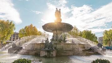 Una fuente con estatuas y chorros de agua, rodeada de árboles y edificios.