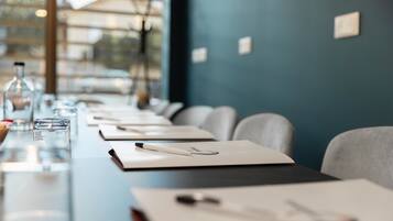 A conference room with a long table, chairs, and a window with a view of buildings.