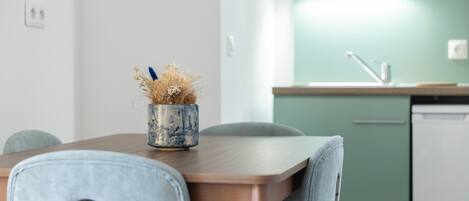 A modern kitchen with a wooden table, a blue vase with dried flowers, and a green wall.