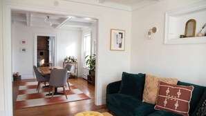 Ein Wohnzimmer mit einem grünen Sofa, einem gelben Hocker und einem Essbereich mit Tisch und Stühlen.