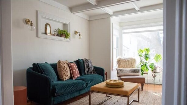 Ein Wohnzimmer mit einem petrolfarbenen Sofa, einem runden Couchtisch und einem kleinen Beistelltisch mit einer Pflanze.