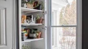Ein Eckzimmer mit weißem Sessel, einer eingebauten Ablage mit Pflanzen und Büchern sowie einem Fenster mit Blick auf ein Gebäude.